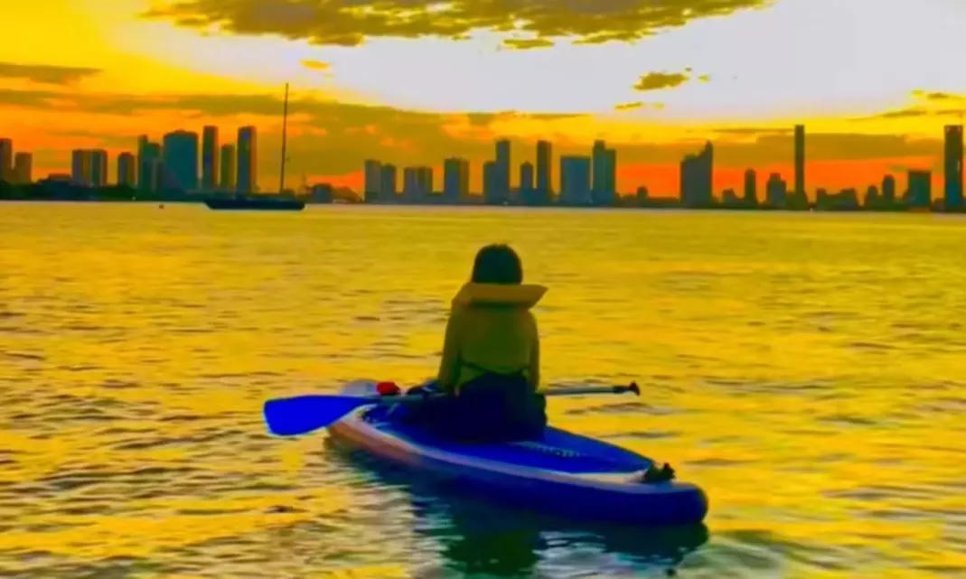 Paddler facing the Miami skyline at sunset